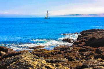 White sailboat in fog on the horizon and massive stones in the foreground, Atlantic Ocean in...