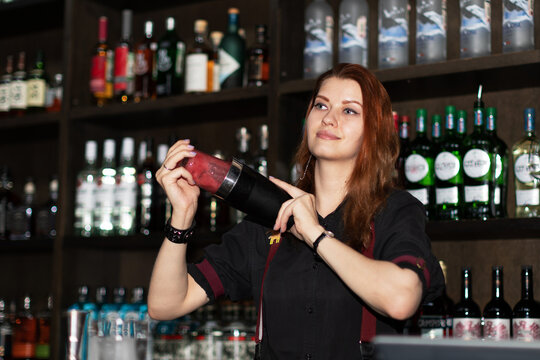 Attractive female bartender with shaker mixing coctail, focus on model
