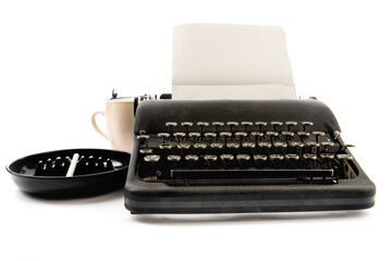 an 1940's era black portable typewriter with an ashtray with a cigarette and a cup of coffee  isolated on white