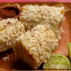 Mexican corn on the cob also called elotes with cheese and mayonnaise on pink background
