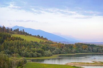 Autumn landscape of a lake shore with colorful trees and blue mountains in the background on sunset
