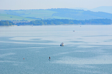Man on paddle board and boat on a lake, hills in a distance