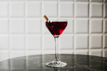 A deep red cocktail in a nick and nora glass garnished with cinnamon