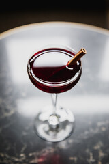 A deep red cocktail in a nick and nora glass garnished with cinnamon