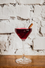 A deep red cocktail in a nick and nora glass garnished with cinnamon