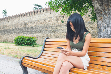 Young sexy girl sits on the bench and holds phone. Social media and dating during pandemic...