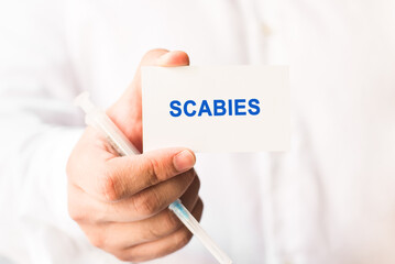 Word scabies on a white background with a syringe in hand. Medicine concept