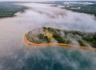 Morning aerial view of lake with fog above water surface and sunrise over forest