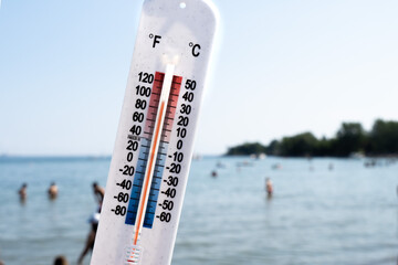 A thermometer held up over a a hot crowded beach, reading about 90 degrees Fahrenheit 30 degrees Celsius
