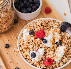 muesli with blueberries and yogurt in a white ceramic bowl standing on a bamboo tray