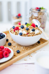muesli with berries and yogurt curd arranged on a wooden tray on the breakfast table with jar and saucers environment