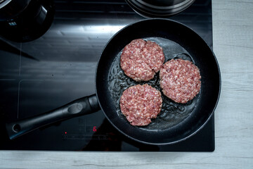 Meat burgers or cutlet-shaped patty being shallow fried in oil on a frying pan in a black plate, close up. Russian or Polish version of cutlets - kotlety. Top view. Flat lay.