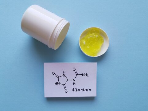 Structural chemical formula of allantoin molecule with comfrey gel in plastic jar. Allantoin is present in botanical extracts of the comfrey plants, stimulates tissue repair and wound healing.