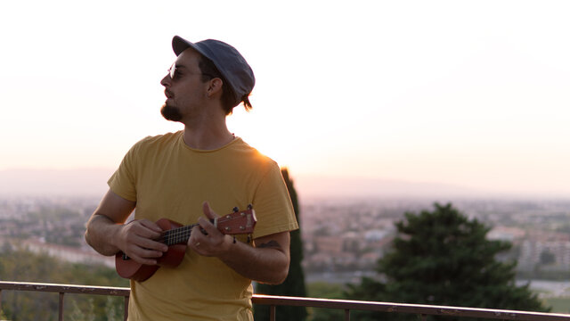 A boy playing the ukulele and the city in the background.