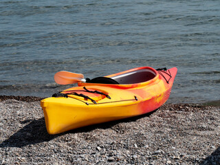  red plastic one man kayak drawn up on a beach by a lake