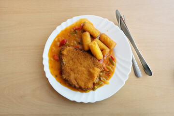 Canteen food cooked from convenience ingredients, breaded schnitzel with bell pepper sauce and potato croquettes on a white plate, copy space, view from above