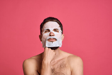 Fototapeta premium Man with bare shoulders in a white mask clear skin pink background