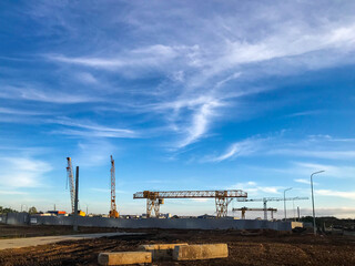 construction cranes stand against the background of a cloudy blue sky. construction site, tunnel digging equipment. yellow gantry crane for transporting heavy concrete materials