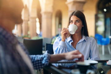 An young carefree romantic happy couple in love is having fun and drinking coffee while enjoying a breakfast together in city center cafeteria on a weekend in a sunny day.