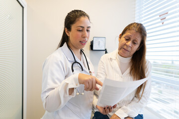 Young latin female doctor with papers explaining exam results to patient at medical clinic health,...
