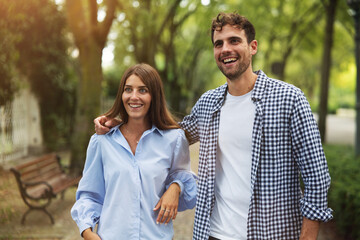 Fototapeta premium Authentic shot of an young happy romantic couple in love is having fun and enjoying time together while taking a walk in a green city park in a sunny day.