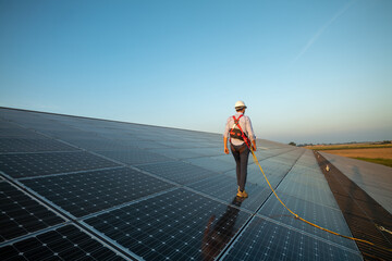 Maintenance assistance technical worker in uniform is checking an operation and efficiency performance of photovoltaic solar panels on roof at sunset.
