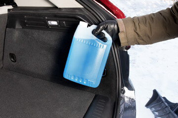 winter driving safety - he driver placing a jug of windshield washer antifreeze in the trunk