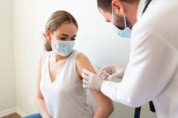 Doctor applying a vaccine on a woman's arm - obrazy, fototapety, plakaty