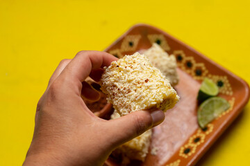 Mexican corn on the cob also called elotes with cheese and mayonnaise on yellow background