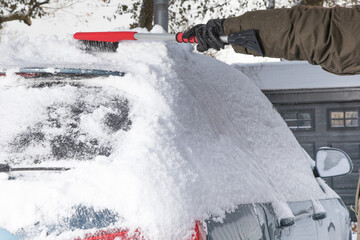 winter driving safety - a driver brushing fallen snow from the roof of the car so it does not blow while driving