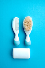 Set of baby accessories for hygiene. Two white hair comb crest brushes with handle for all types white soap, isolated on blue copy space background. flat lay.Top view.