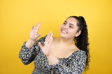 Young beautiful woman with curly hair over isolated yellow background scared with her arms up like something falling from above