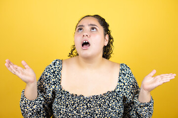 Young beautiful woman with curly hair over isolated yellow background  crazy and mad shouting and...