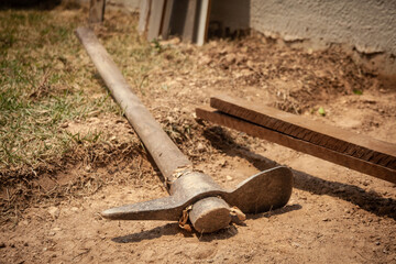 ferramenta picareta jogada ao  ch&atilde;o de uma obra com  grama e madeira ao fundo