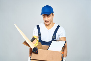 man in working uniform with a box in his hands tools loader delivery light background