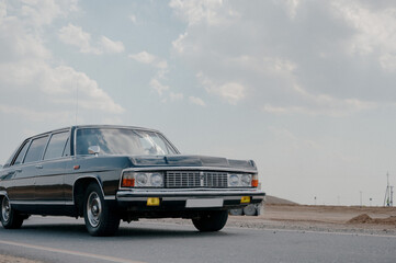 Obraz na płótnie Canvas Black luxury retro car.Soviet retro car close up.retro car in black color at the minimalistic background of desert terrain and blue sky.