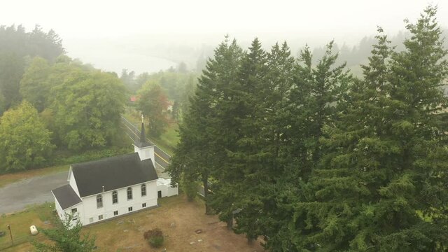 Aerial View of a Little White Church on a Foggy Morning. Atmospheric look at a Congregational Church and the accompanying graveyard with a view to the Salish Sea in the background.