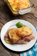 Scalloped potatoes with ham and cheese on wooden background