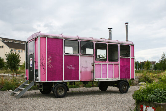 An old, broken-down caravan truck, with its panels painted several different colours of pink, under a flat grey sky.  Image has copy space.