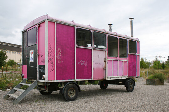 An old, broken-down caravan truck, with its panels painted several different colours of pink, under a flat grey sky.  Image has copy space.