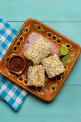 Fototapeta na wymiar Mexican corn on the cob also called elotes with cheese and mayonnaise on turquoise background