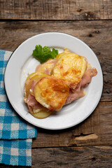 Scalloped potatoes with ham and cheese on wooden background