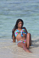 Young Hispanic woman looking her body lying on sand Caribbean beach with turquoise sea around