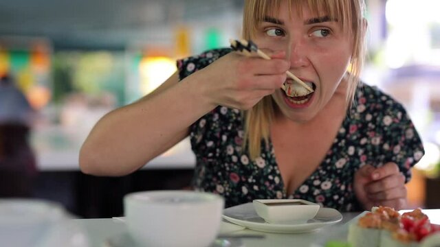 Happy woman eating sushi rolls in restaurant