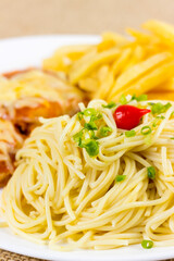Spaghetti with slices of chive and spice. Chicken with cheese and french fries. Selective focus