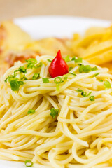 Spaghetti with slices of chive and spice. Chicken with cheese and french fries. Selective focus