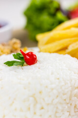 Rice with chicken filet and french fries on a white plate with a raw cotton dish towel. Selective focus