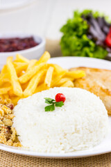 Rice with chicken filet and french fries on a white plate with a raw cotton dish towel. Selective focus