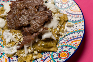 Mexican green chilaquiles with cecina beef steak on pink background