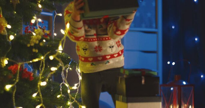 Cute Caucasian little child wearing a Santa hat having x-mas present at the Christmas tree at night.
